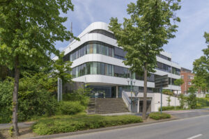 Das Bild zeigt ein großes, beleuchtetes Gebäude in dunkler Umgebung. Helle Lichtlinien verlaufen über die Fassade und betonen ihre Struktur. Der Hintergrund ist dunkel, sodass die Beleuchtung besonders auffällt.